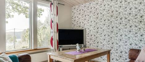 Una sala de estar acogedora con techo de madera, un ventanal grande, un televisor, una mesa de madera y un tapete estampado.