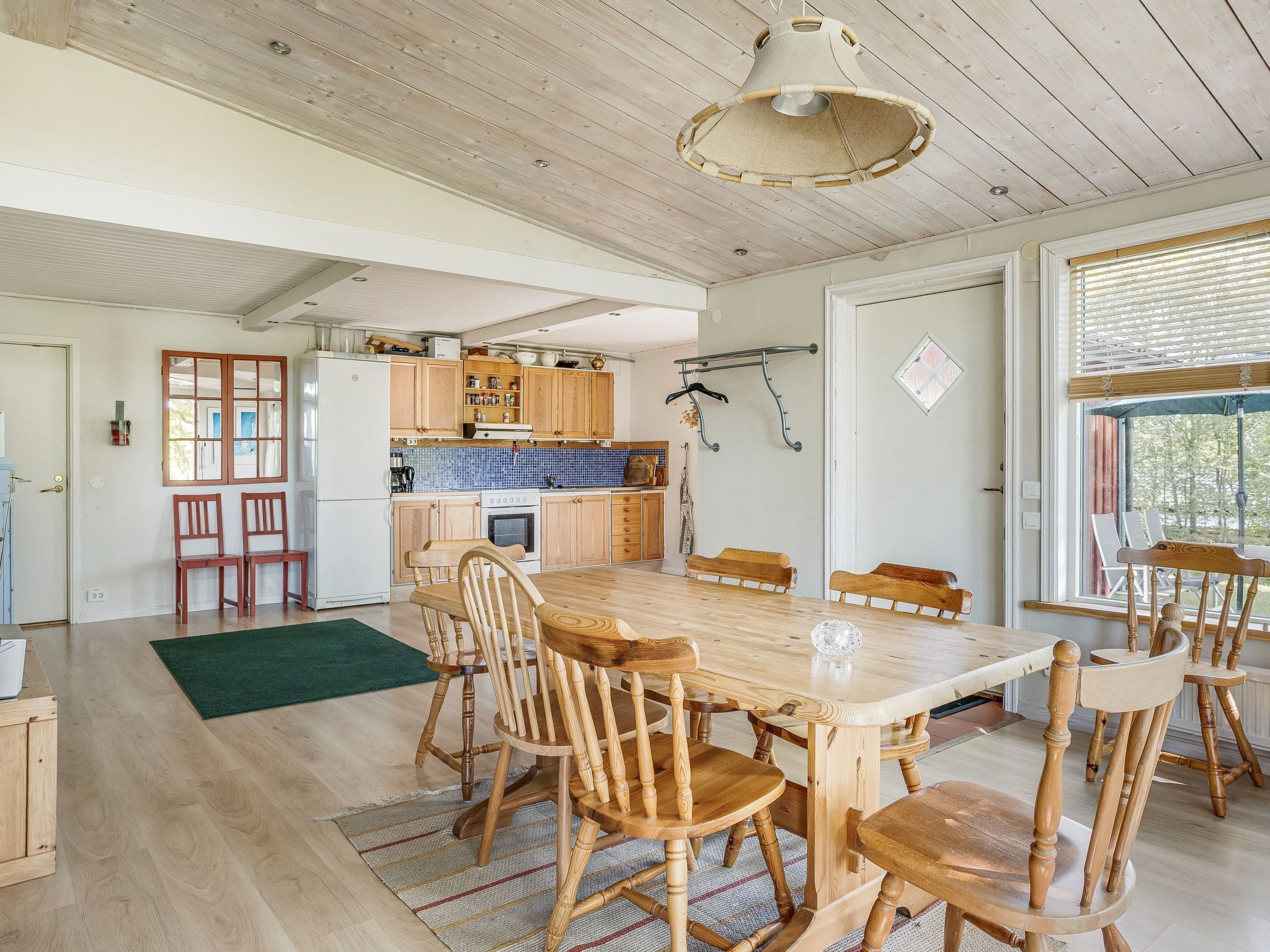 A spacious kitchen with wooden cabinets, a dining table with wooden chairs, and a hanging light fixture.