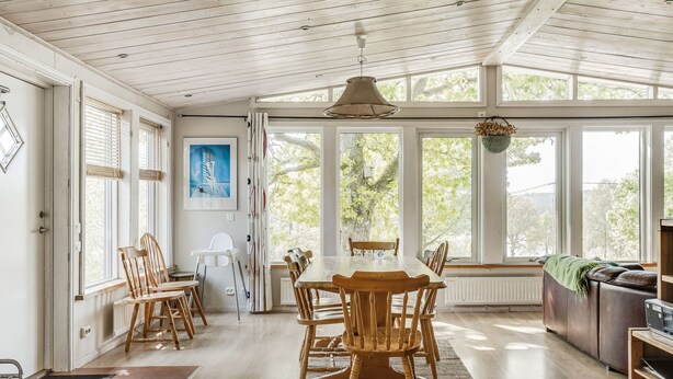 A spacious dining area with a wooden table and chairs, large windows, and a view of trees.