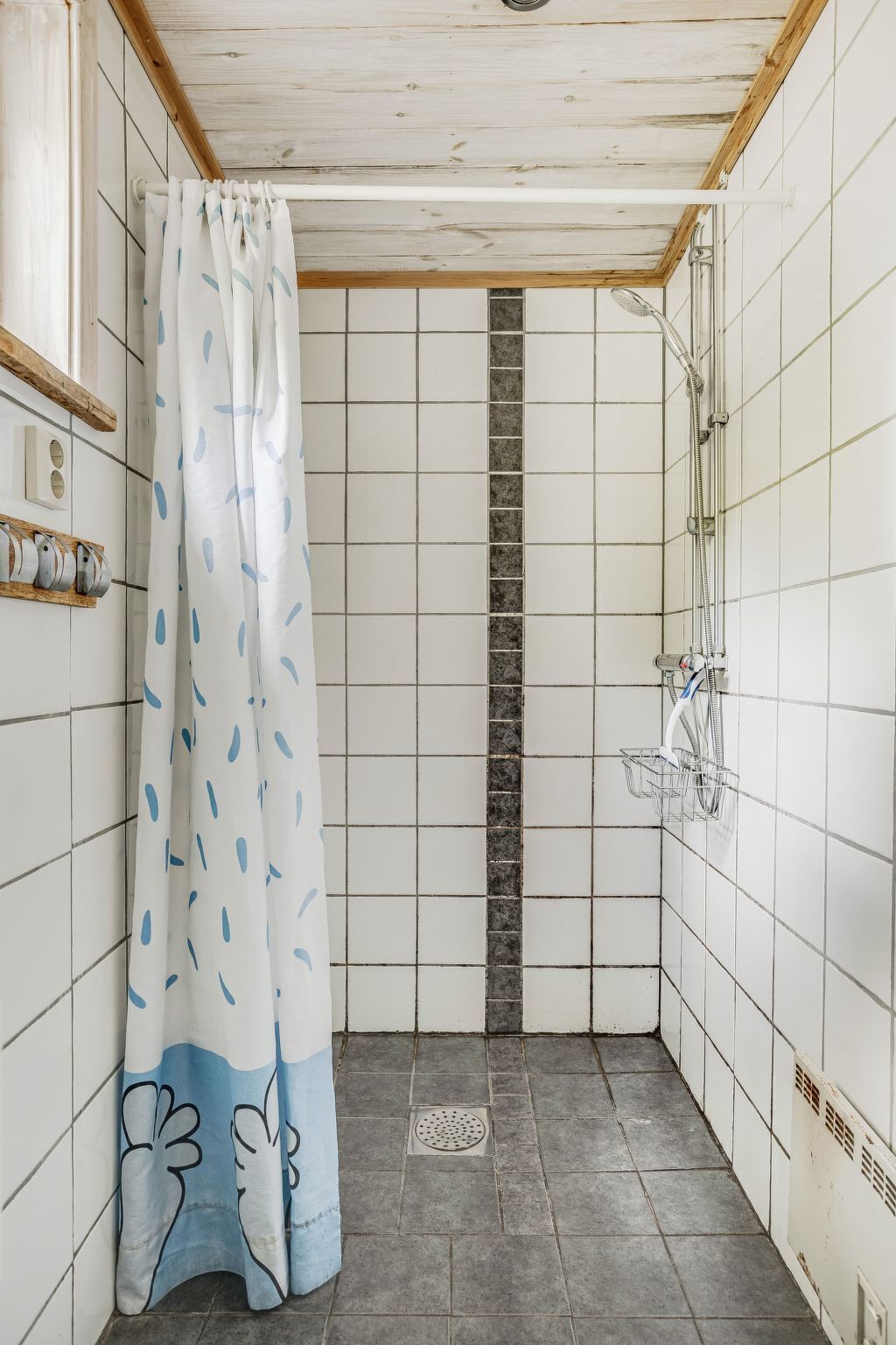 A small, tiled shower area with a shower curtain featuring a blue and white abstract pattern.