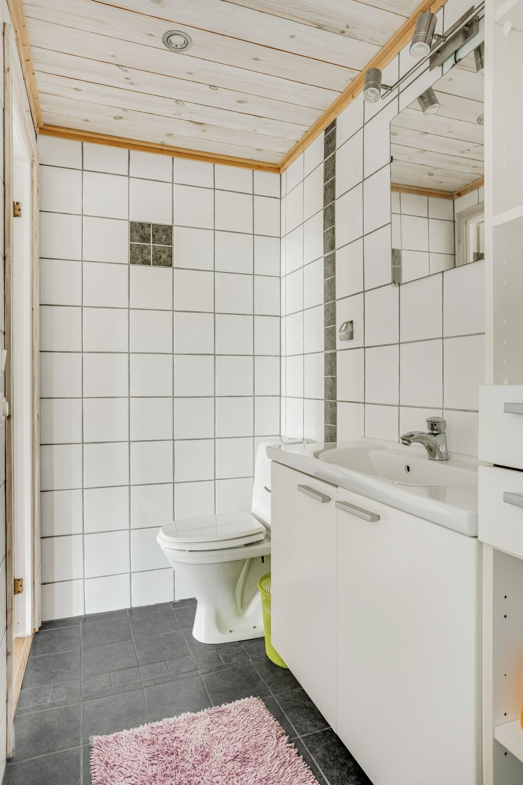 Une salle de bain moderne avec des carreaux blancs, des toilettes, un lavabo et un miroir.