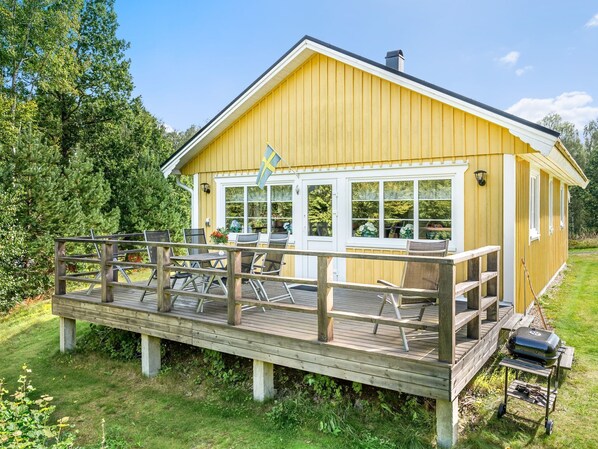 A yellow wooden cabin with a deck, outdoor seating, and a grill. - Gaslunda by Interhome (Olofström)