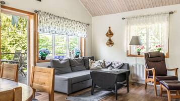 Un salon chaleureux avec un canapé gris, une table à manger en bois et une table basse noire. On y trouve deux fauteuils, une lampe et une fenêtre avec des rideaux.