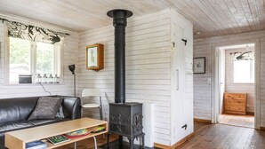 Ett mysigt rum med en svart vedeldad kamin, en lädersoffa, ett träbord och en inramad tavla på väggen.