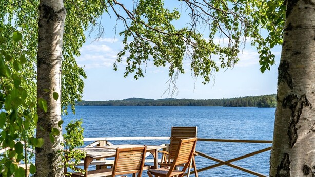 Terraza de madera con dos sillas y una mesa, con vistas a un lago.