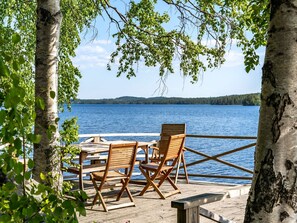 A wooden deck with two wooden chairs and a table overlooking a lake.