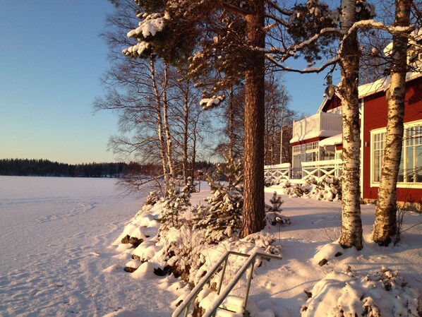A snow-covered landscape with a red building, bare trees, and a clear sky.