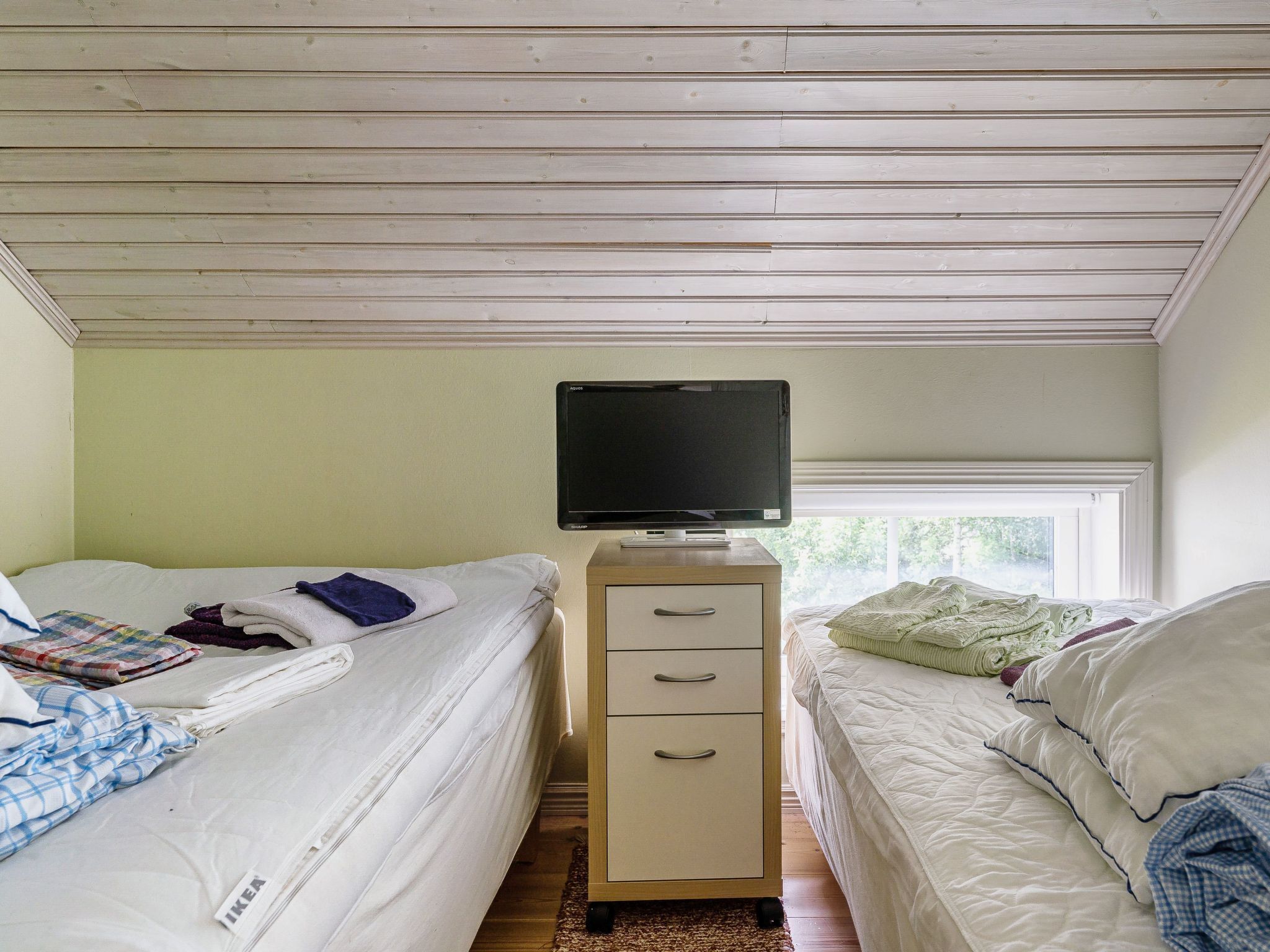 Une chambre avec deux lits, un téléviseur posé sur un meuble et une fenêtre qui laisse entrer la lumière naturelle.