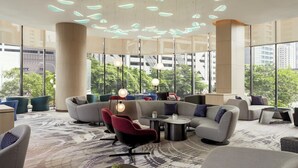 A modern lounge area with sofas, chairs, and tables, large windows offering views of the city, and a unique ceiling light design. - Holiday Inn Kuala Lumpur Bangsar by IHG (Kuala Lumpur)