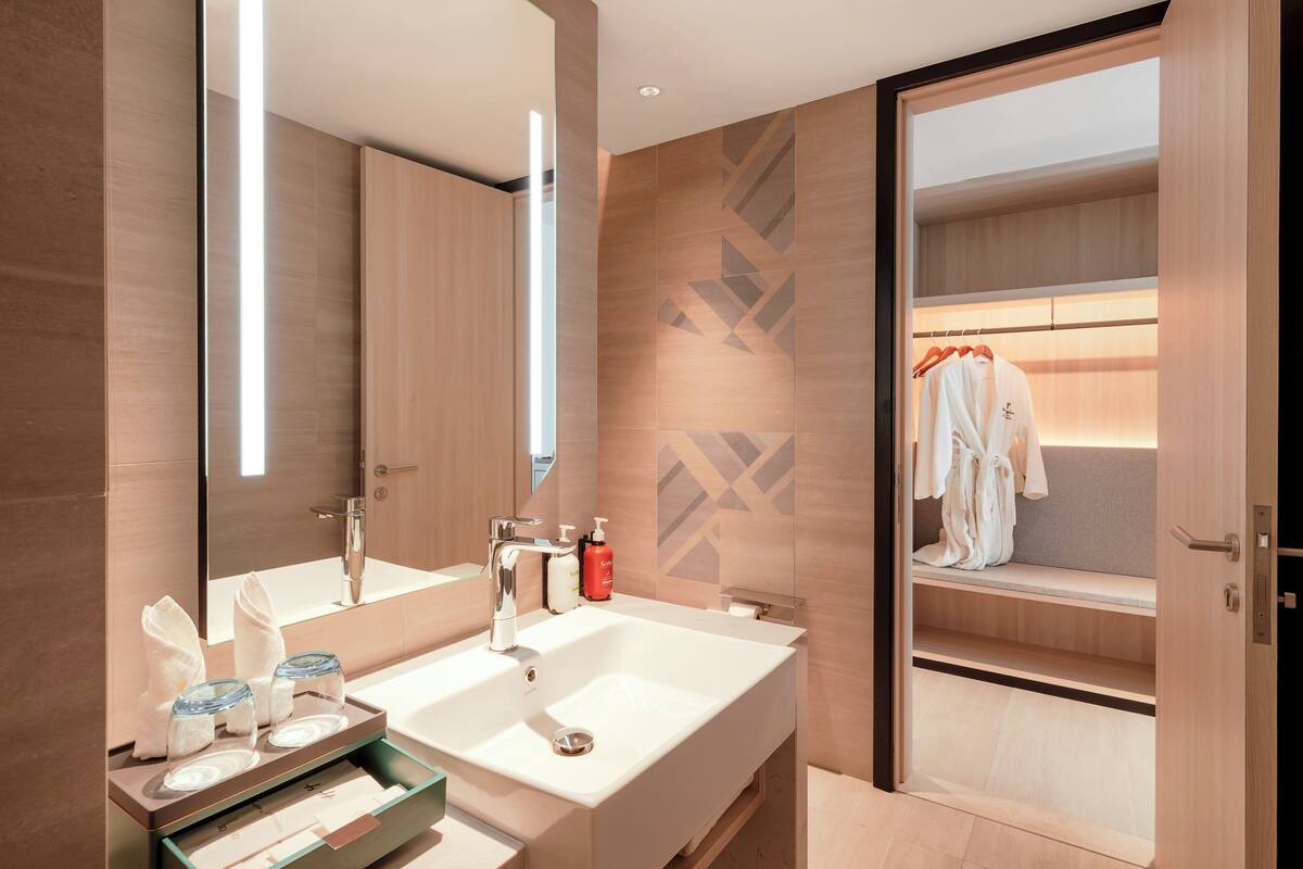 A modern bathroom with two sinks, a large mirror, and a robe-wrapped bench.