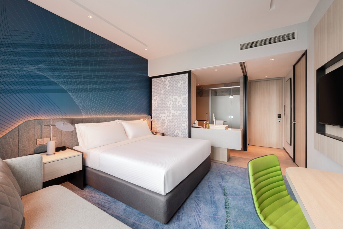 A modern hotel room with a large bed, a desk, a chair, and a TV.