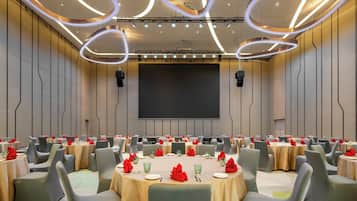 A conference room with multiple tables, chairs, and a large screen.