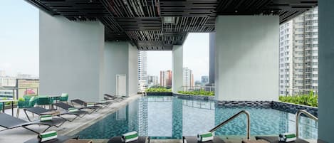 A rooftop swimming pool with lounge chairs and a view of the cityscape.
