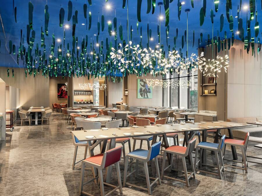 A spacious restaurant with high ceilings, hanging light fixtures, and a variety of seating arrangements.