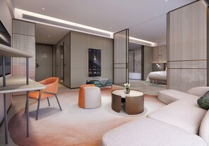 Ein modernes Hotelzimmer mit einer Couch, einem runden Couchtisch, einem Esstisch mit einem Stuhl und einem Bett.