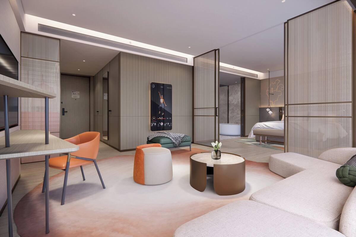 A modern hotel room with a sofa, a round coffee table, a dining table with a chair, and a bed.