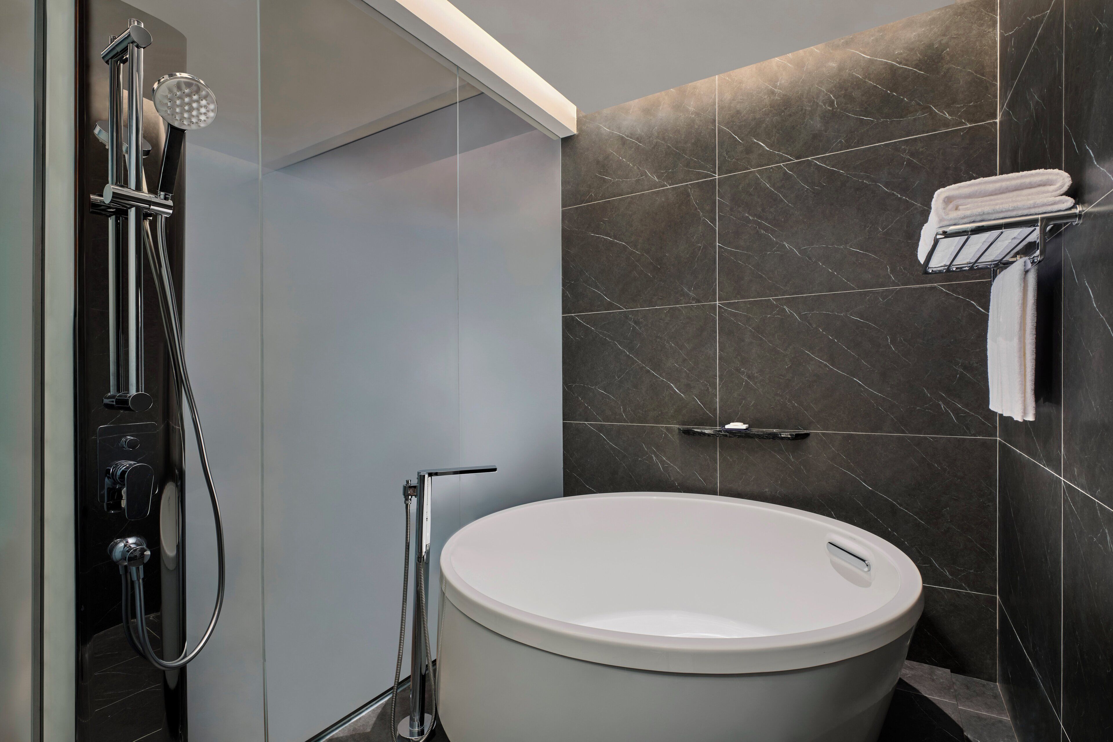 A modern bathroom with a freestanding bathtub, a handheld showerhead, and a towel rack.