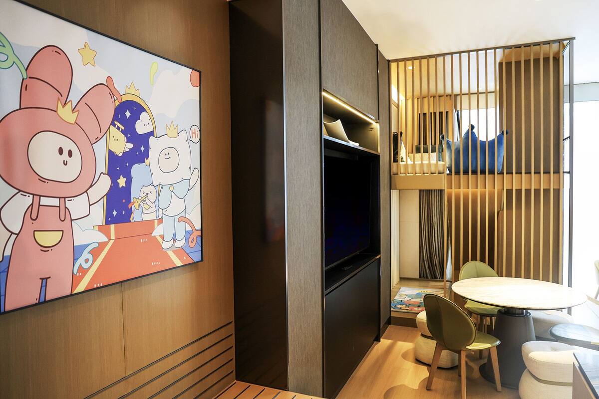 A modern room with a large wall mural, a flat-screen TV, a round table with chairs, and a window with blinds.