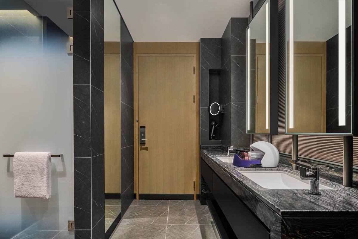 A modern bathroom with a wooden door, a large mirror, a marble sink, and a towel rack.