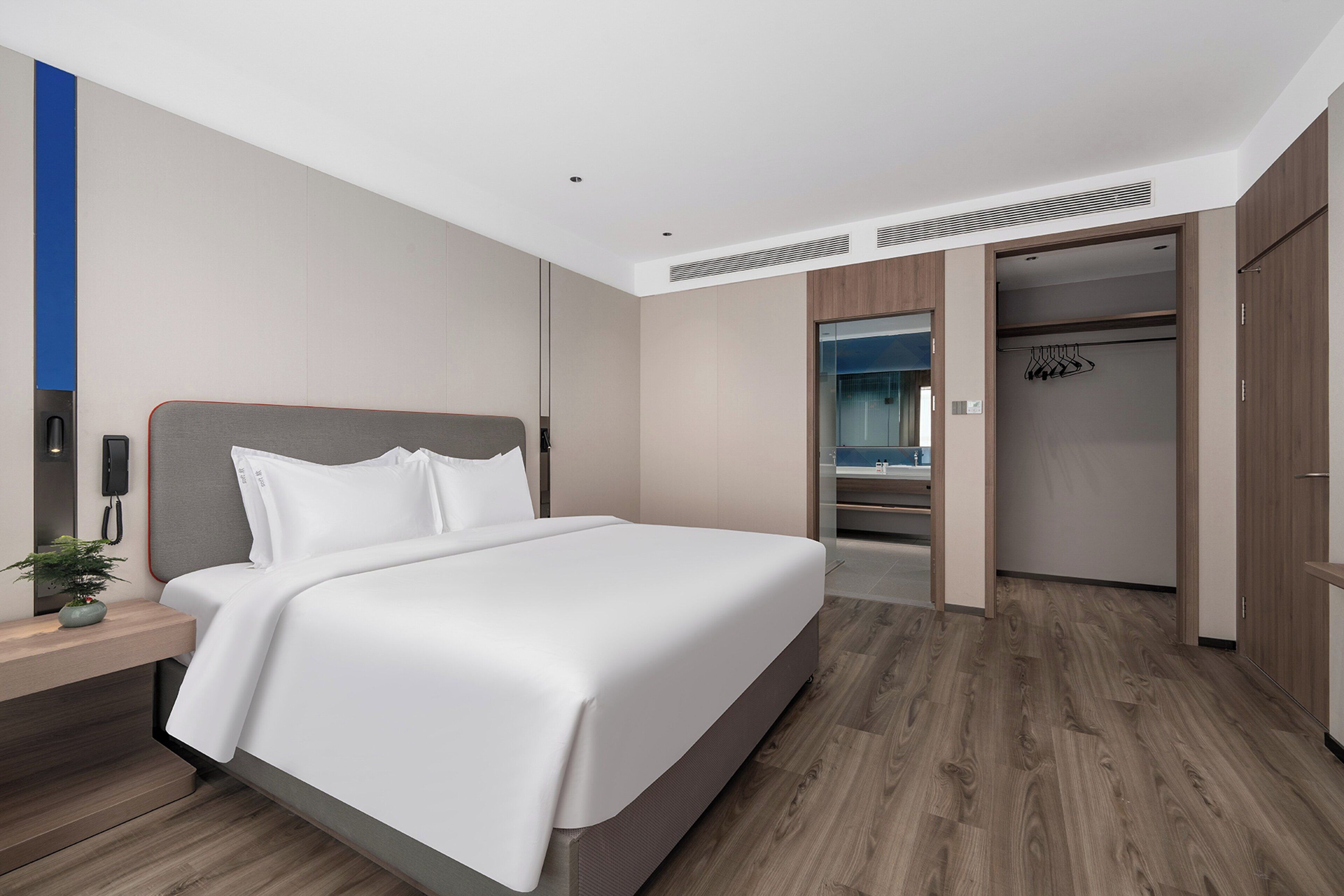 A modern hotel room with a large bed, a bedside table with a lamp, and a view of the bathroom through an open door.