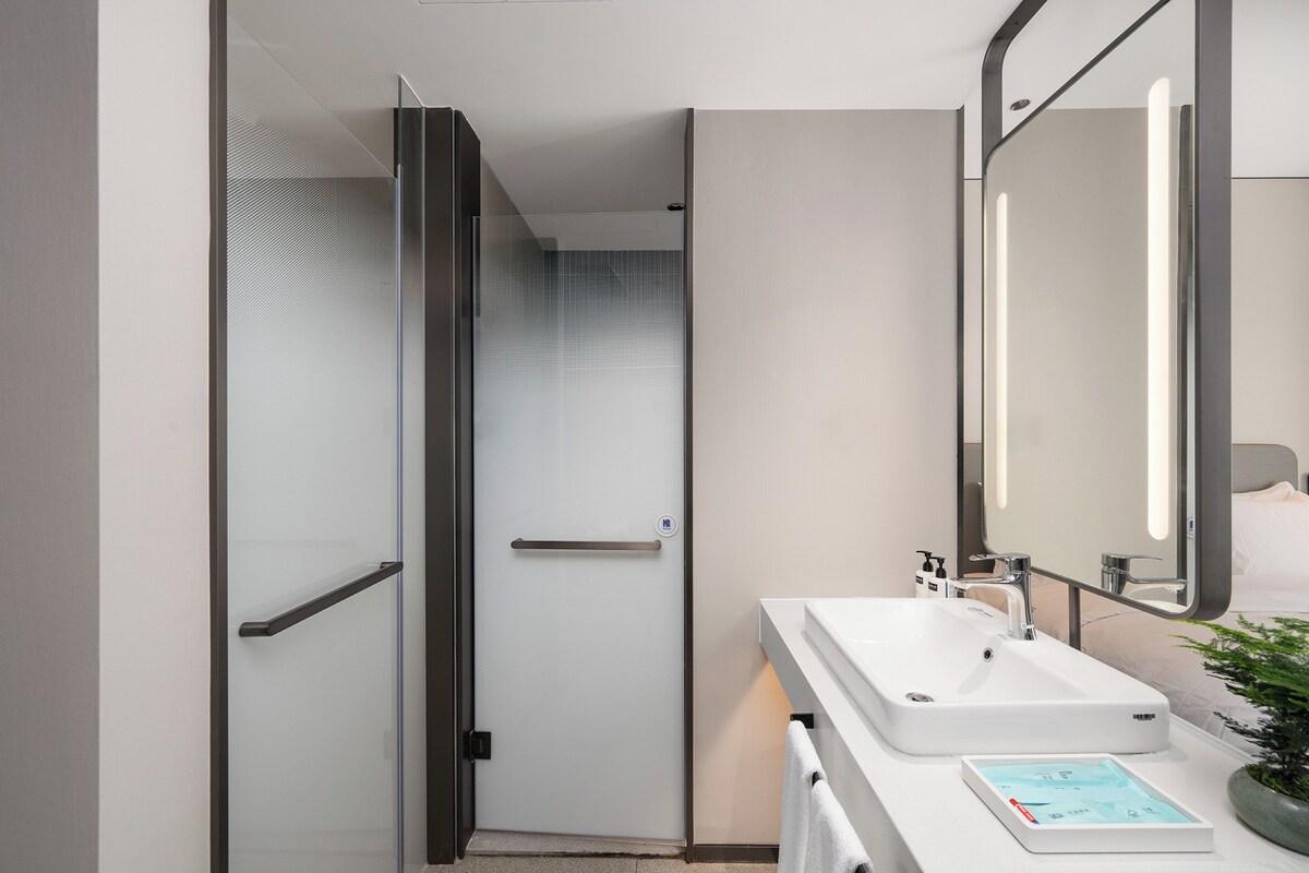A modern bathroom with a glass shower door, a white sink, and a mirror.