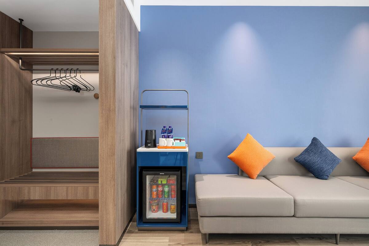 Ein gemütlicher Raum mit integriertem Minikühlschrank, einer Sitzecke mit Kissen und einem an der Wand befestigten Wäschetrockner.