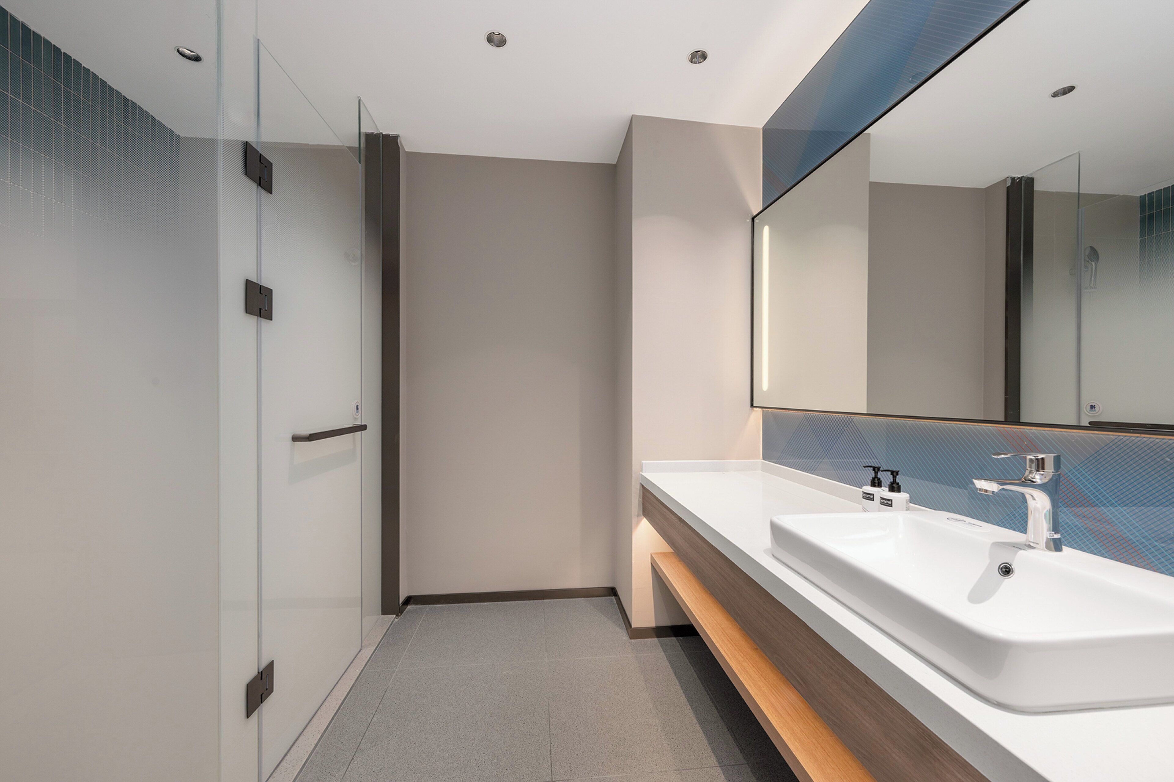 A modern bathroom with a glass shower enclosure, a large mirror, and a dual sink vanity.