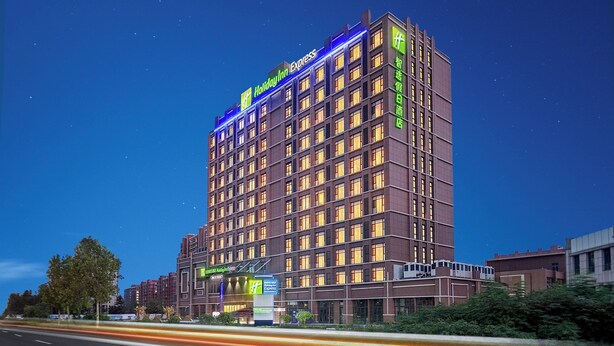 A multi-story Holiday Inn Express hotel with a modern design, featuring a prominent signage and uniform window lighting. - Holiday Inn Express Qingdao Hongdao Station by IHG (Qingdao)