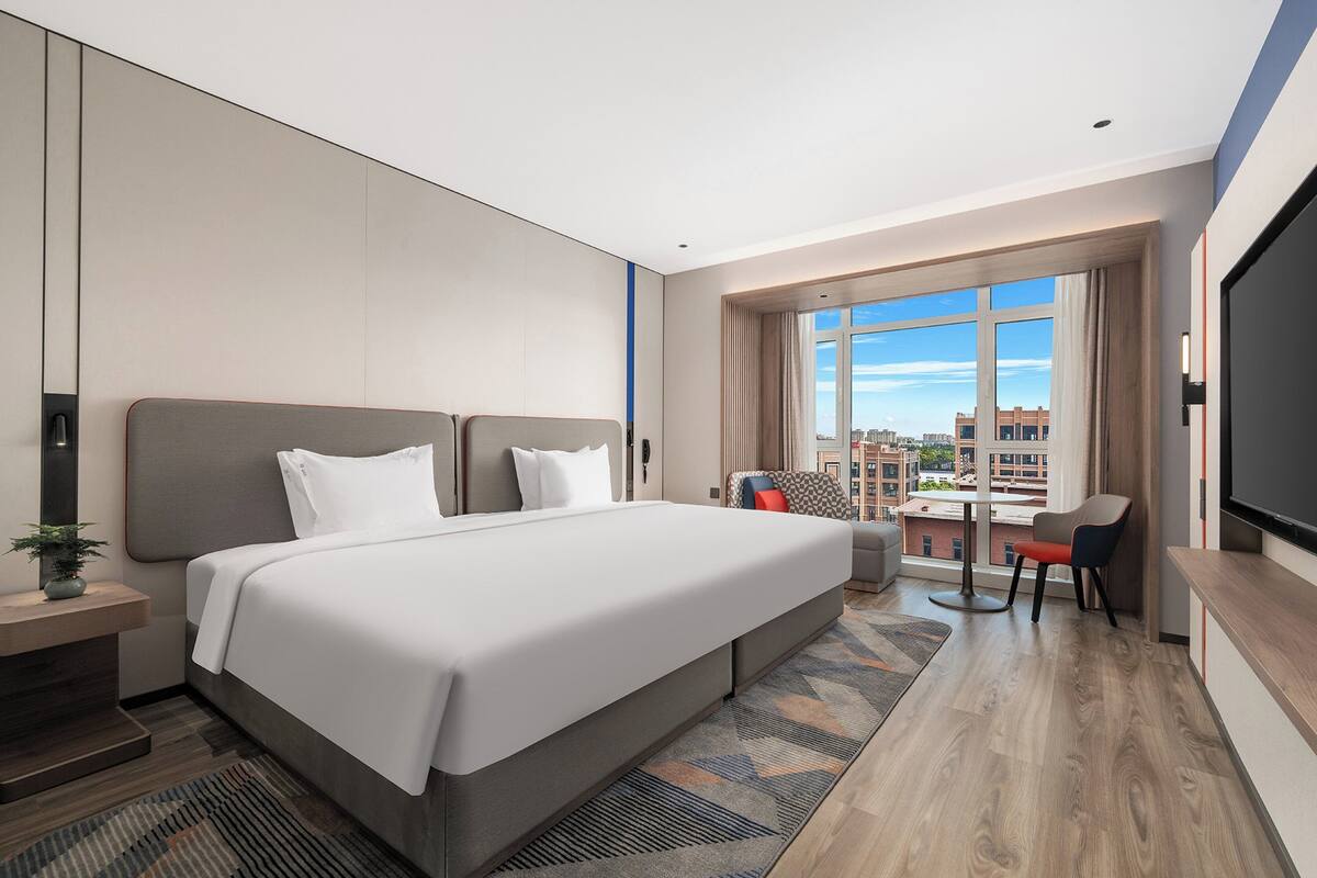 Ein modernes Hotelzimmer mit einem großen Bett, einem Schreibtisch und Blick auf die Stadt.