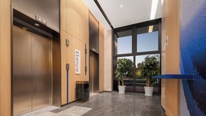 A modern elevator with a directory sign, a marble floor, and large windows with a view of buildings and trees. - Holiday Inn Express Qingdao Hongdao Station by IHG (Qingdao)