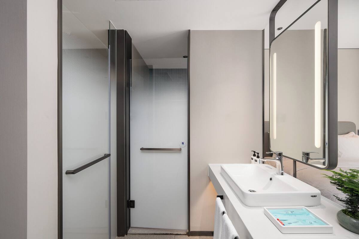 Ein modernes Badezimmer mit Duschabtrennung aus Glas, einem weißen Waschbecken und einem Spiegel.