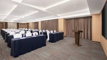 A conference room with rows of tables, white chairs, and a podium.