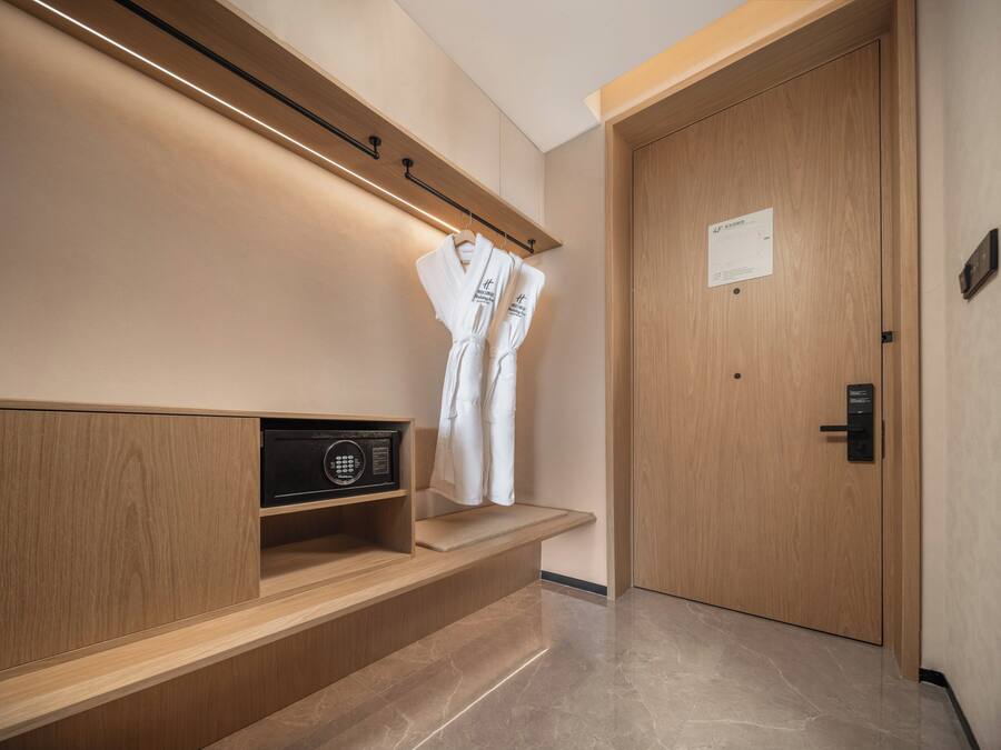 A modern hotel room with a wooden bench, a robe hanging on a hook, and a door with a sign.