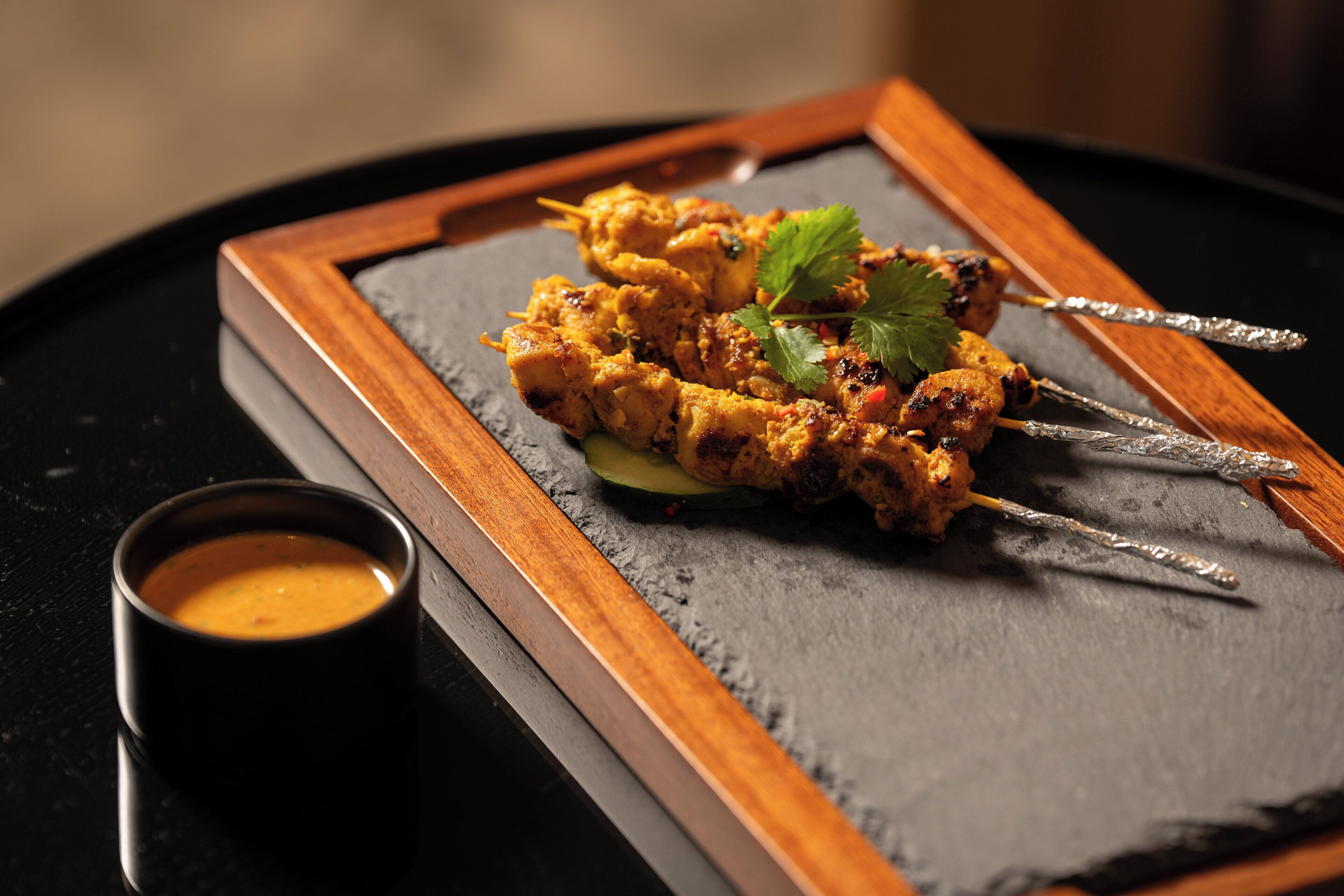 A plate of grilled chicken skewers with a side of sauce and a wooden frame.