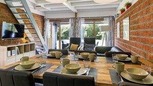 A modern dining area with a brick wall, a wooden table set for four, and a TV mounted on the wall. - De Schans by Interhome (Lauwersoog)