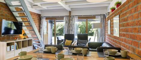 A modern dining area with a brick wall, a wooden table set for four, and a TV mounted on the wall.