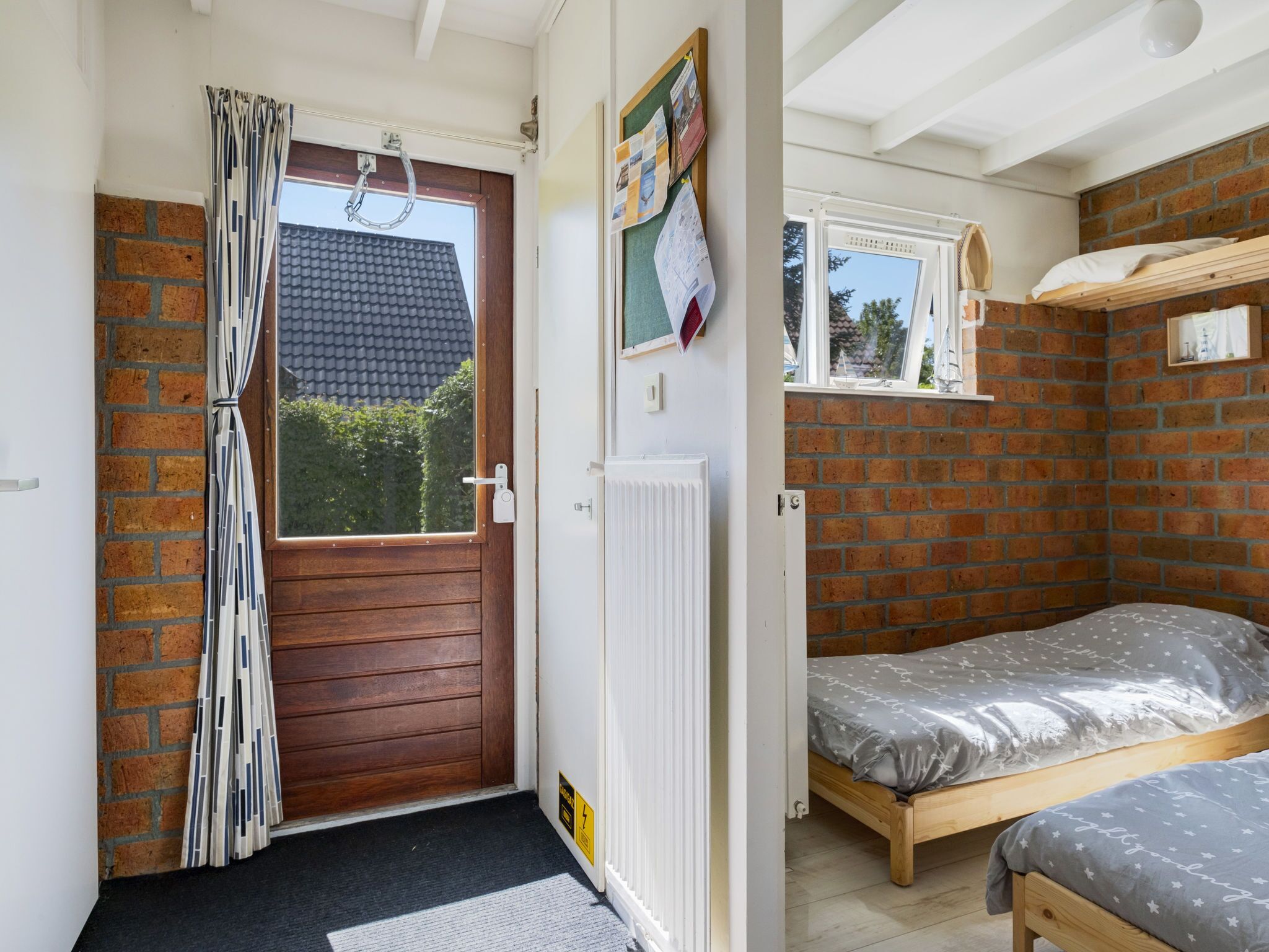 A compact room with a wooden door, a small window, a radiator, and a bed with a grey patterned bedspread.