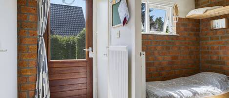 A compact room with a wooden door, a small window, a radiator, and a bed with a grey patterned bedspread.