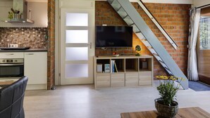 A modern living room with a TV, wooden cabinets, a staircase, and a kitchen area with a brick wall. - De Schans by Interhome (Lauwersoog)