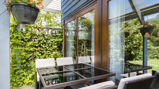 A patio with a glass-top table and wicker chairs, surrounded by greenery and a wooden fence. - De Schans by Interhome (Lauwersoog)