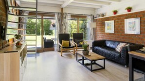 A modern living room with a black leather sofa, two armchairs, a wooden coffee table, and a bookshelf filled with books. Large windows provide a view of the outdoors. - De Schans by Interhome (Lauwersoog)