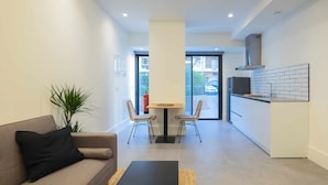 A modern apartment with a living area featuring a sofa, a coffee table, and a dining table with chairs. There is a kitchen area with a stove and a tiled backsplash. - Apartamento Presidente 1 (Sevilla)
