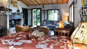 Un salon chaleureux avec une cheminée, un canapé, une table avec des livres et des jeux de cartes, et une lampe.
