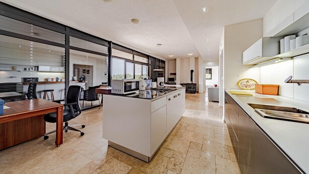 A modern kitchen with a central island, a dining area with a wooden table, and a view of the outdoors through large windows.