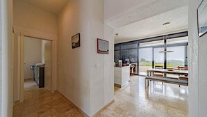 A modern kitchen with a large window, a dining area with a bench, and a hallway leading to a door.