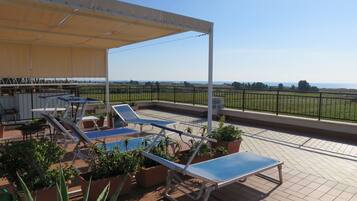 Una terrazza con lettini, un tavolo e piante in vaso.