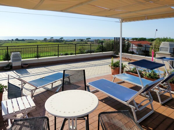 A covered outdoor patio with a table and chairs, a ping pong table, and potted plants.
