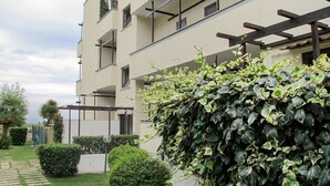 Een meerlaags woongebouw met balkons, een tuin met hagen en een heldere lucht.