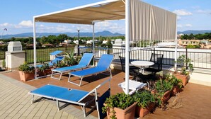 Een dakterras met blauwe loungestoelen, een tafel en potplanten.