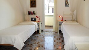 Een kamer met twee éénpersoonsbedden, een klein bureau met een lamp, een boekenkast en een deur naar buiten.